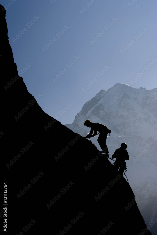 Grimpeurs en contre jour sur un massif rocheux en arrière plan de massif du Mont Blanc