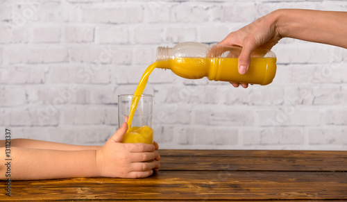 Mother pouring her son some orange juice in glass from bottle