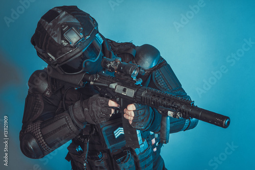 Member of the SWAT squad with an assault rifle in a black uniform on blue background. Special weapons and tactics. Special Forces.
