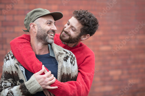Gay couple cuddling and laughing in front of brick wall