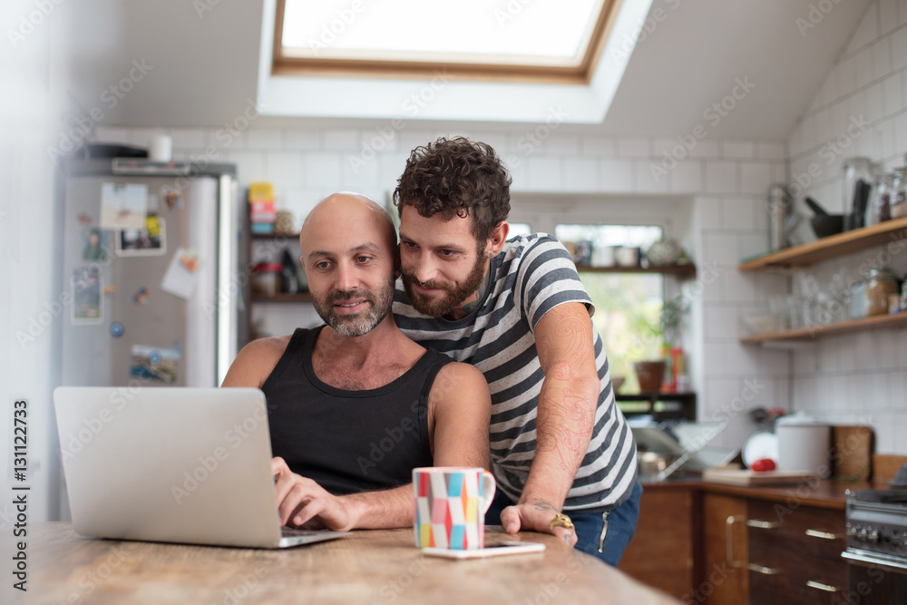 Gay couple using laptop in the kitchen Gay couple using laptop in the kitchen
