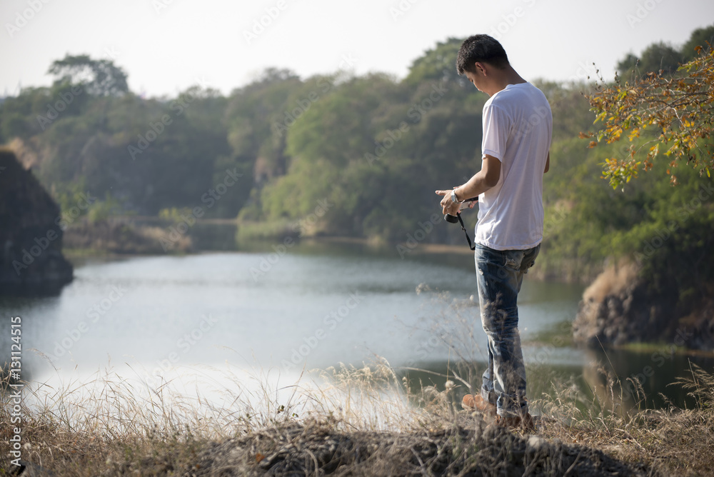Handsome guy wearing white t-shirt and jeans, holding a camera at mountain peak,lake front Handsome guy wearing white t-shirt and jeans, holding a camera at mountain peak,lake front