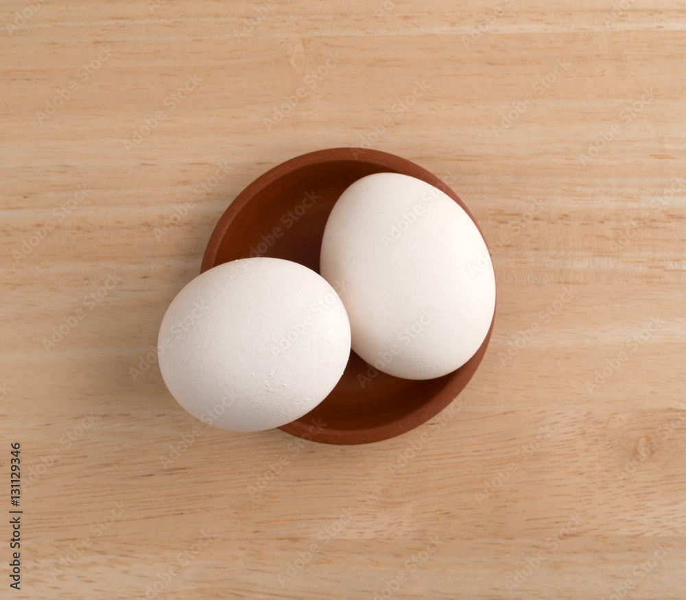 Two eggs in a small bowl atop a wood table. Two eggs in a small bowl atop a wood table.