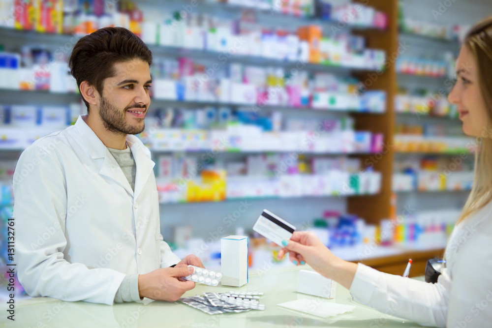 Experienced pharmacist counseling female customer in modern pharmacy, and woman pay with credit card
