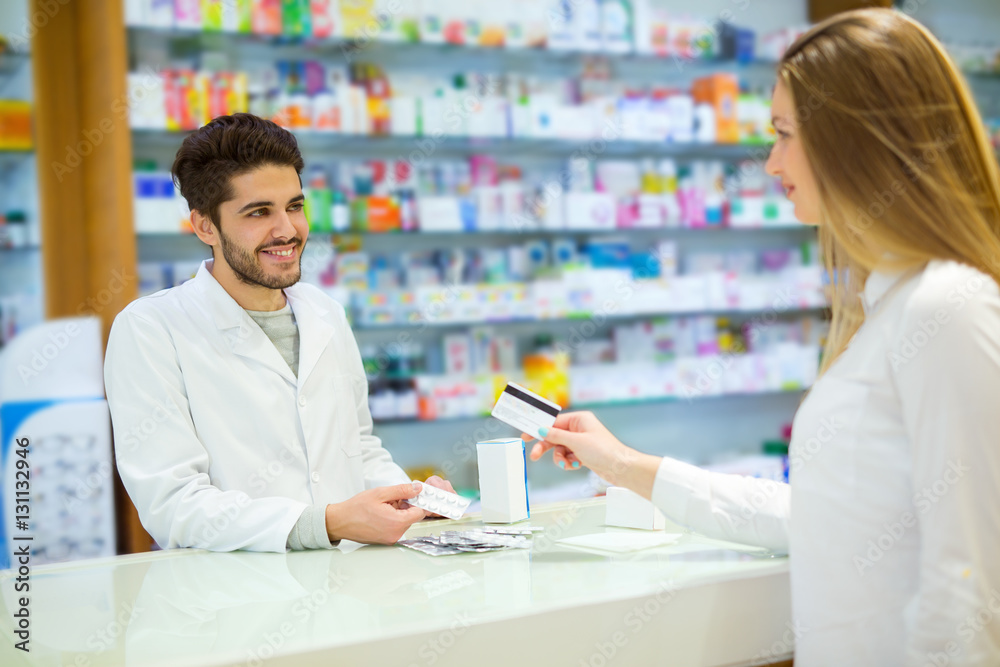 Experienced pharmacist counseling female customer in modern pharmacy, and woman pay with credit card