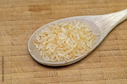 Reiskörner in einem Kochlöffel auf einem Küchenbrett photo
