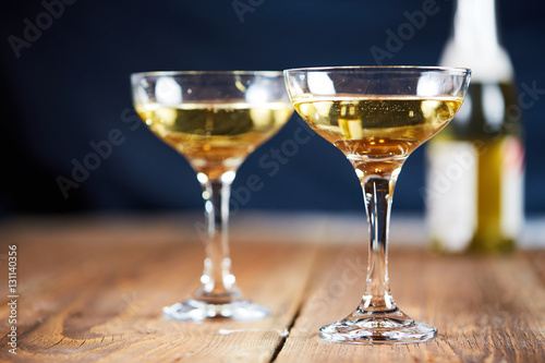 Two glasses of champagne in front of bottle on wooden table