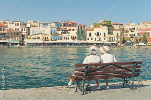 two elderly people sitting on bench looking at city view