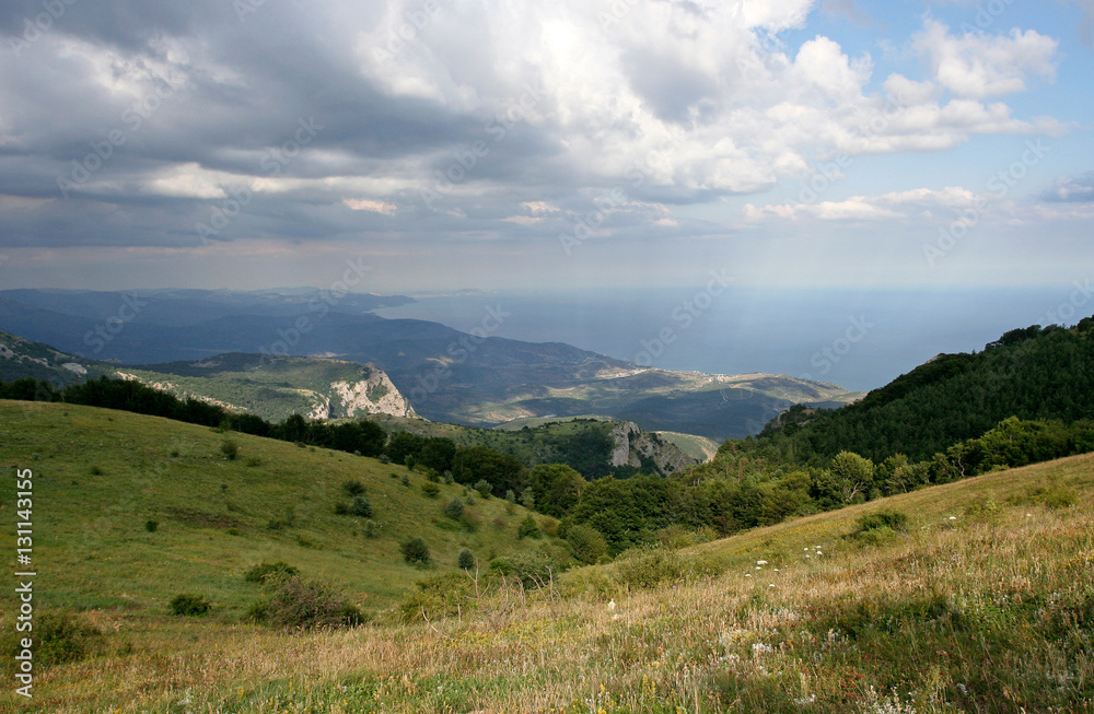 The mountain landscape with green hillsides, distant mountains, far Black sea and sunbeams. This photo was taken in Crimean Mountains, on South Demerdzhi mountain. The mountain landscape with green hillsides, distant mountains, far Black sea and sunbeams. This photo was taken in Crimean Mountains, on South Demerdzhi mountain.