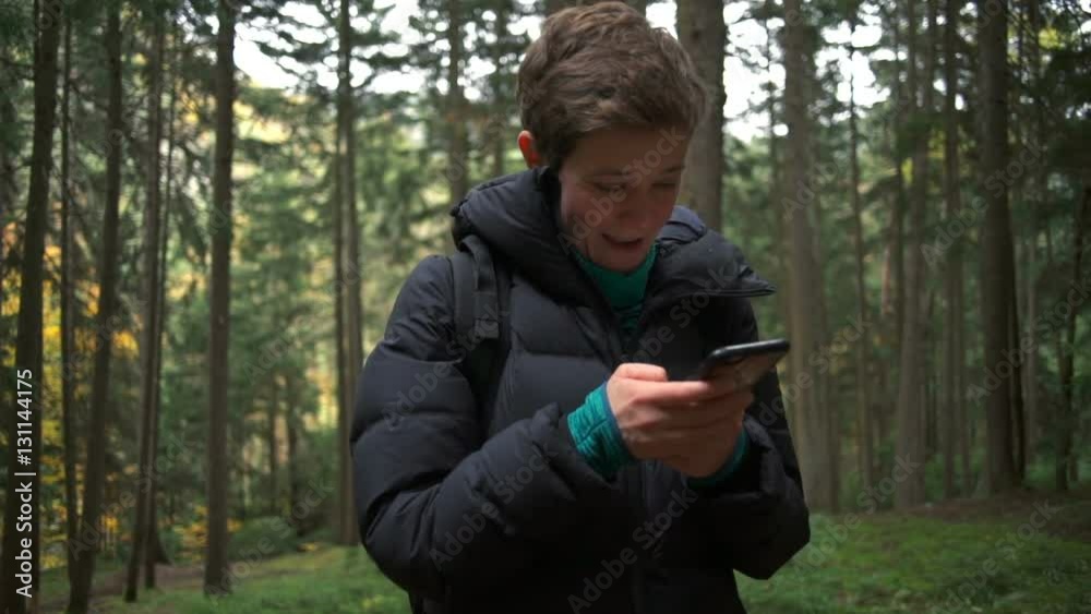 A woman standing with a smartphone in her hand and smiling in a beautiful forest A woman standing with a smartphone in her hand and smiling in a beautiful forest