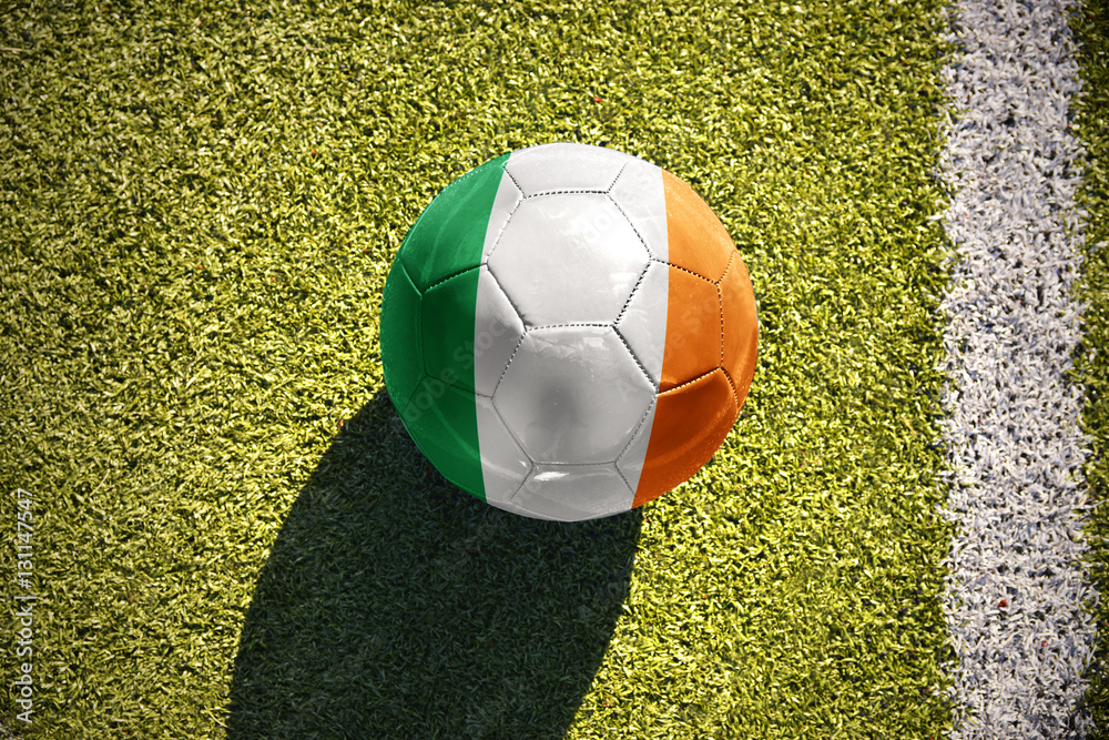 Obraz premium football ball with the national flag of ireland lies on the field