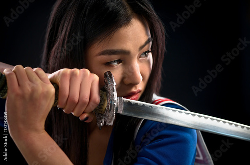 Portrait of pretty brunette lady with red lips looking like warrior. Asian lady posing sword for photographer in studio. photo