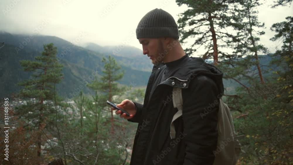 A young handsome man standing in a forest and using his smartphone slow motion A young handsome man standing in a forest and using his smartphone slow motion