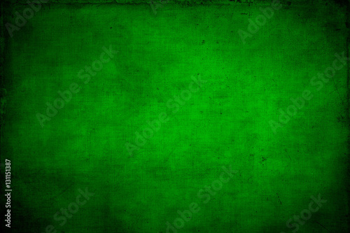 Abstract textured bright green or Christmas background with bright center spotlight and black vignette border. With a vintage grunge background texture.