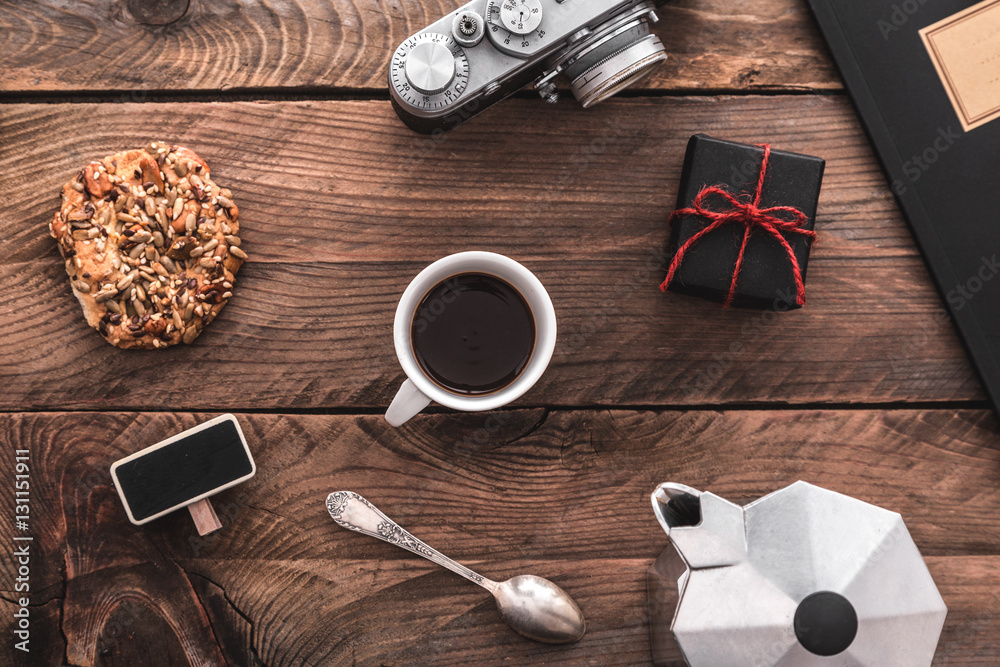 Office desk with photo camera, coffee cup, small gift, coffee maker,  cookies and small chalkboard. Stock Photo | Adobe Stock