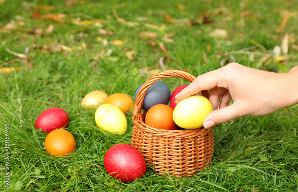 Woman hand taking Easter egg from basket on green grass