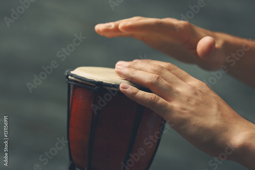 Hands of man playing African drum on blurred grey background, close up