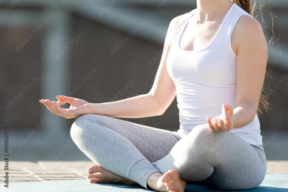 Close up of young woman practicing yoga, in Easy Seat exercise, Sukhasana pose, working out, wearing sportswear, outdoor, sunny summer day background