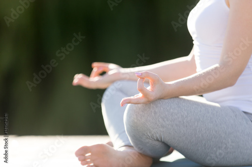 Young woman practicing yoga, sitting in Easy Seat exercise, Sukhasana pose, working out, wearing sportswear, outdoor, park background. Close up of hand