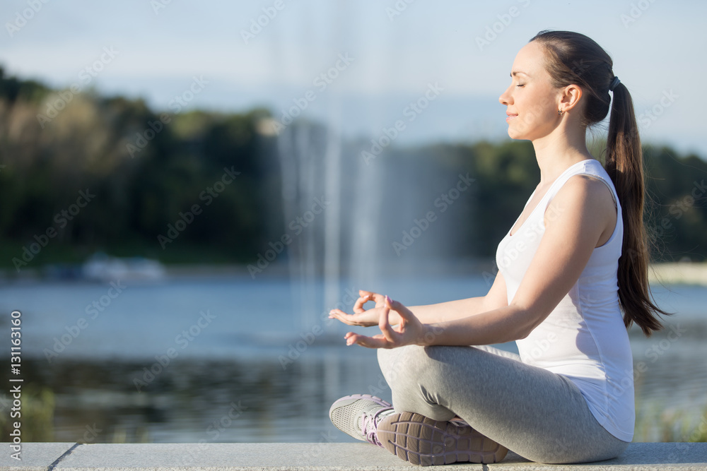 Φωτογραφία Profile portrait of sporty beautiful young woman practicing yoga, sitting in Easy Seat exercise, Sukhasana pose, working out, wearing sportswear, outdoor full length, fountain background