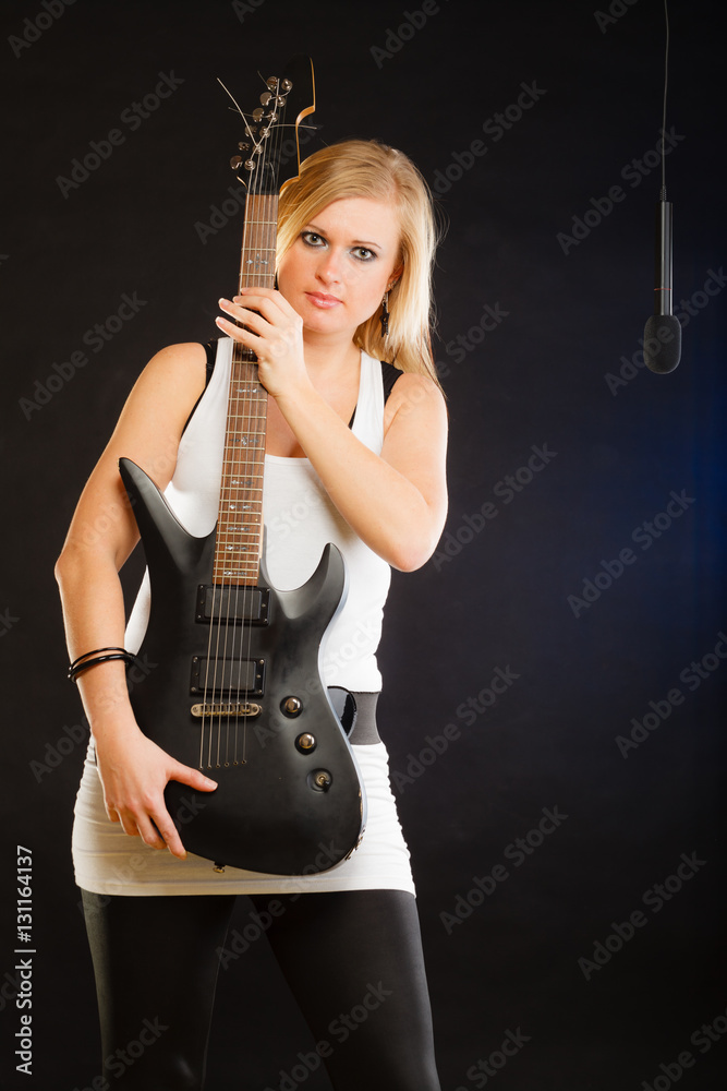 Fototapeta premium Blonde woman holding electric guitar, black background