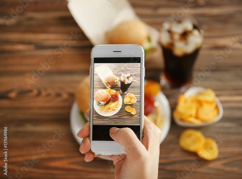 Female hands taking photo of tasty burger with snacks on table