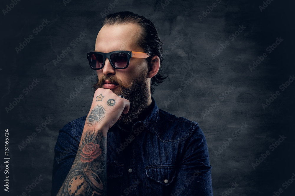 Fototapeta premium Thoughtful bearded male in sunglasses with tattoos on his arms.