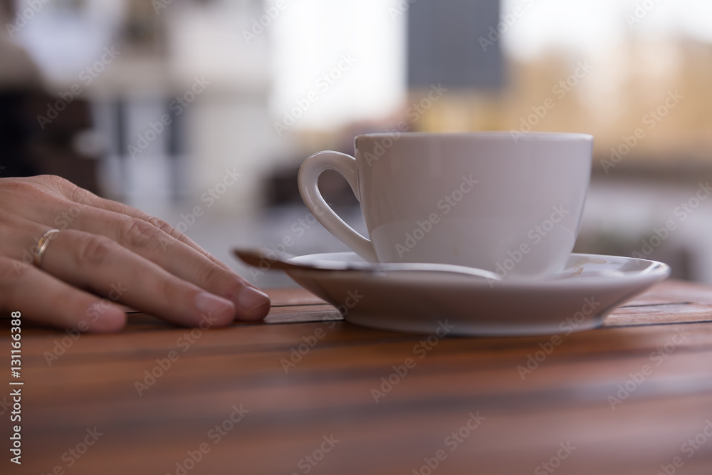 Hand of a young man on a wooden table in the cafe with cup of cocup of coffee in calm relaxing hand's posture,outdoor blur background