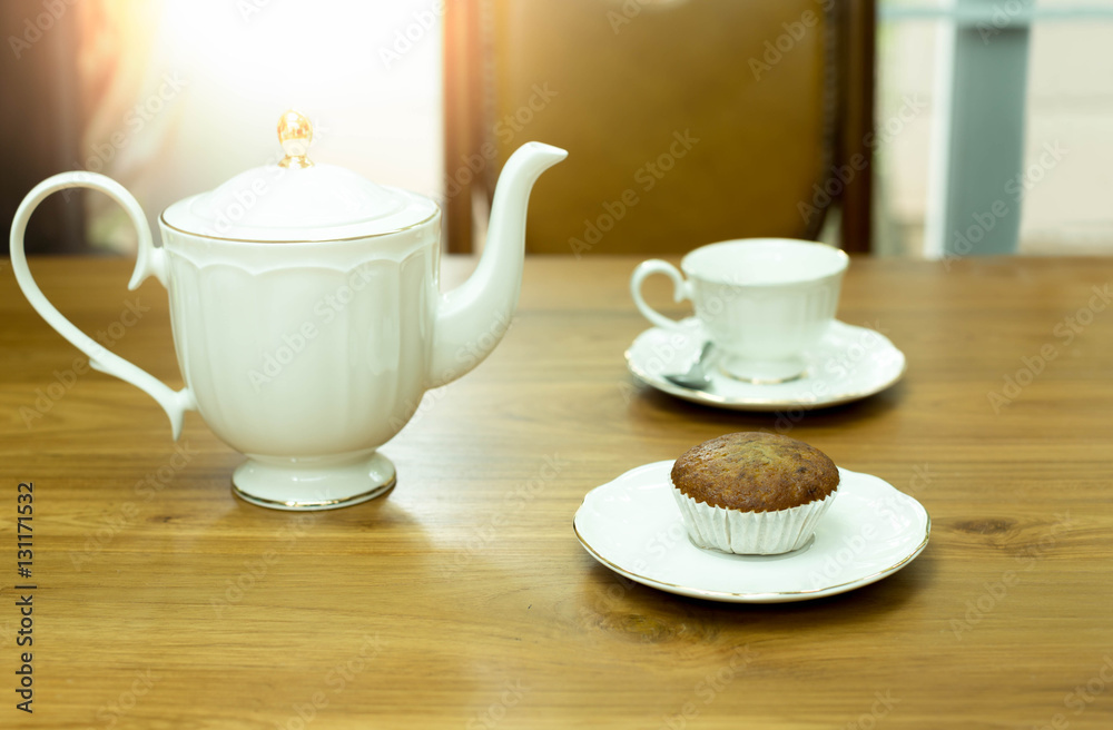 Muffin cake with cup of tea and teapot on wooden table
