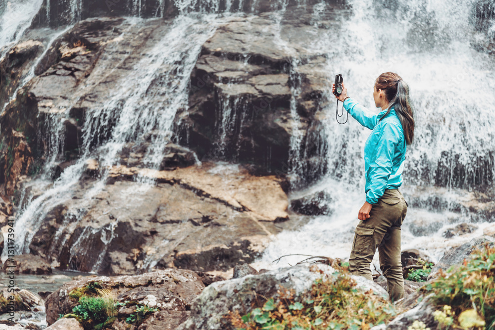 Traveler woman searching direction with a compass near the waterfall