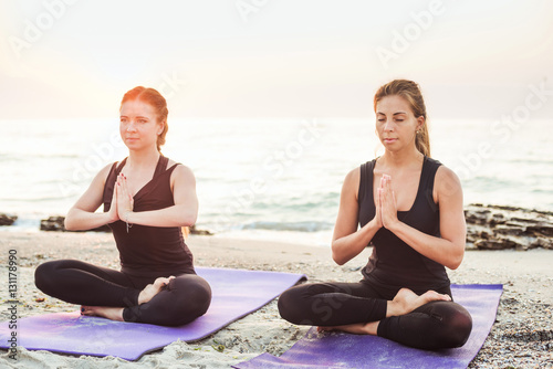 two young caucasian females practicing yoga on beach 