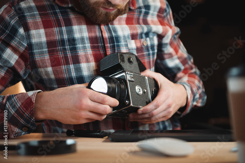 Young engineer fixing vintage camera while sitting at his workplace