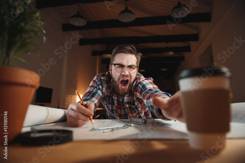 Man worker trying to reach cup of coffee and yawning