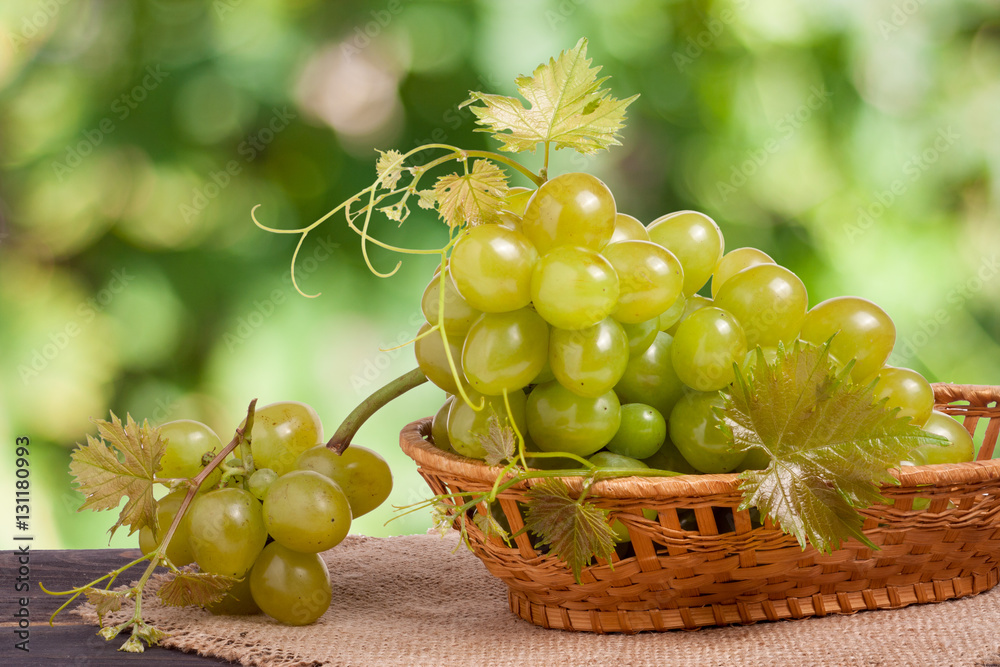 green grapes in a wicker basket on wooden table with blurred background green grapes in a wicker basket on wooden table with blurred background