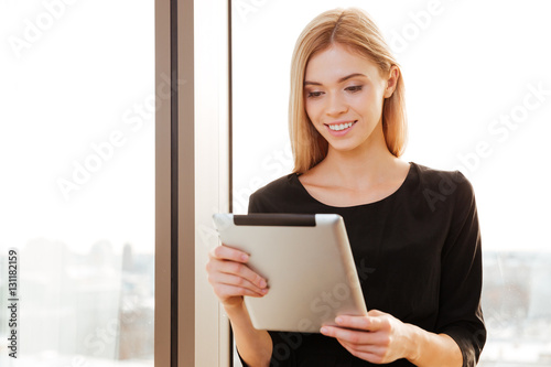 Joyful young lady worker in office holding tablet computer