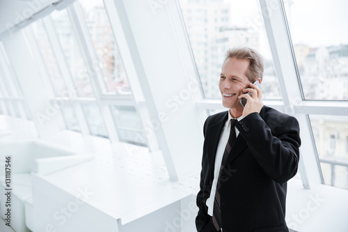Elderly business man talking at phone near the window