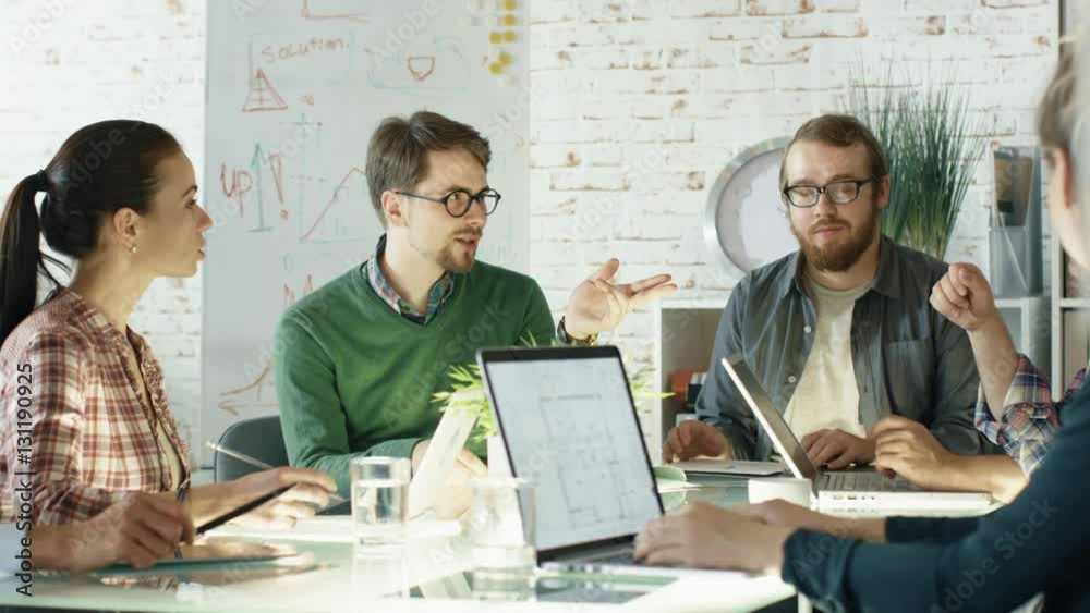 Group of Young Creative People Have Strategic Planning Session. They are Sitting at Big Glass Table with Open Laptops in their Bright and Modern Loft Office. Shot on RED EPIC (uhd). 