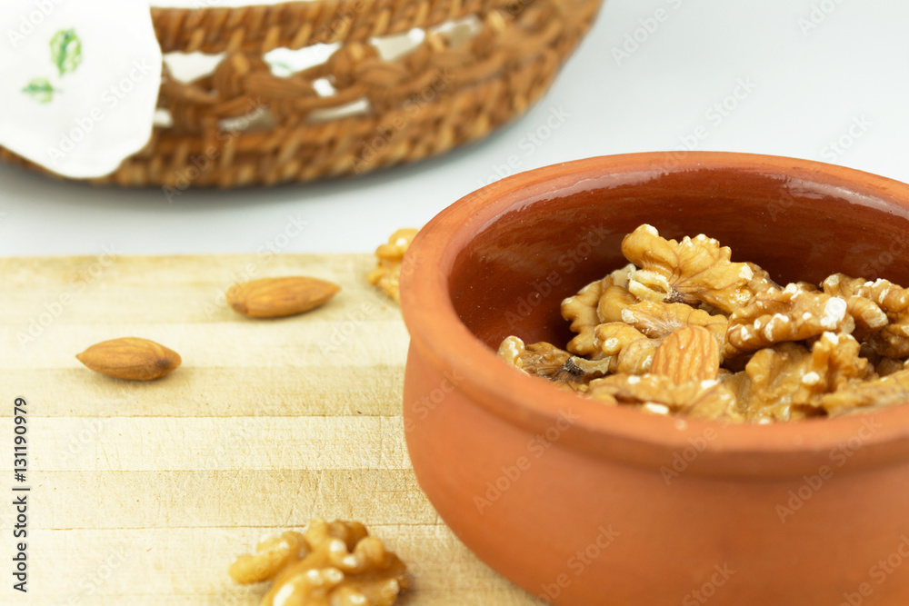 Wallnuts and almonds in earthenware pot on wooden chopping board with basket in frame Wallnuts and almonds in earthenware pot on wooden chopping board with basket in frame