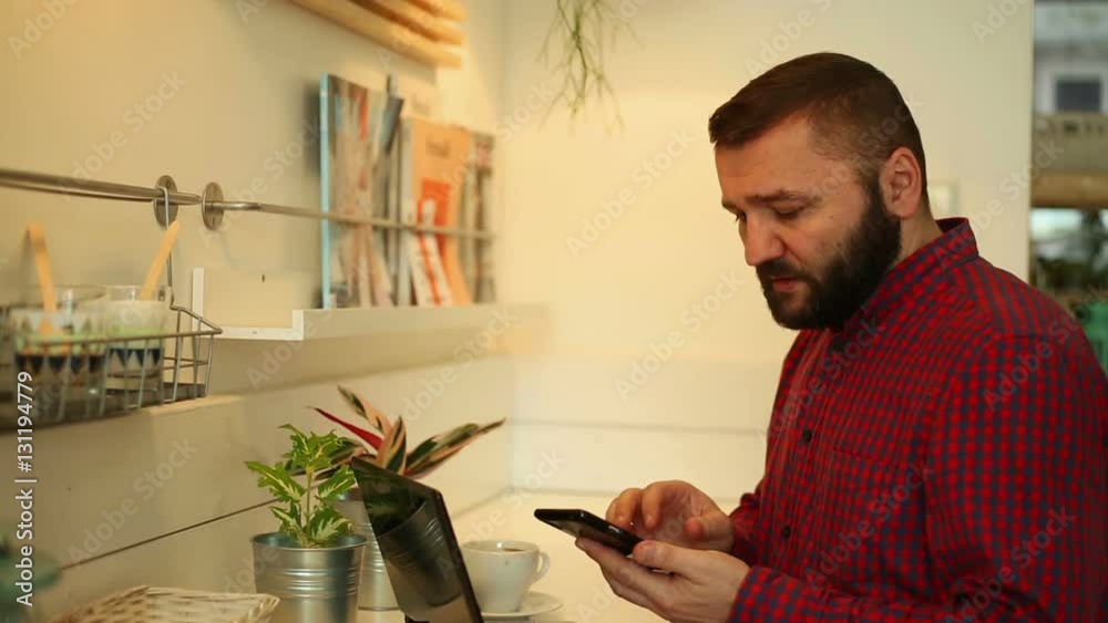 Young man checking something on laptop while talking on the phone in cafe Young man checking something on laptop while talking on the phone in cafe