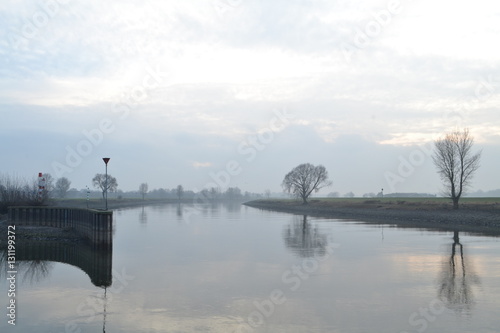 Fotografia De rivier de IJssel stroomt op een nevelige dag langs de haven van Doesburg