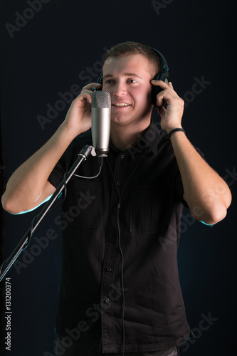 Young guy singing in the studio microphone on dark background
