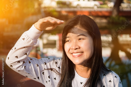 Beautiful asian woman holding her hand above her eyes, shielding face from the sun's rays	