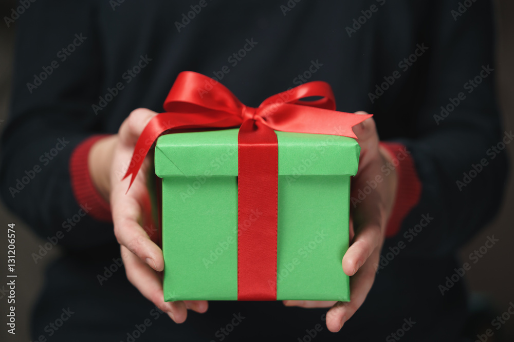 female teen hands show green paper gift box with red bow
