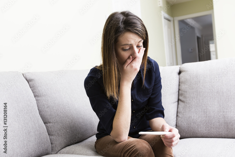 girl sitting on a couch at home while reading the results of her recent pregnancy test girl sitting on a couch at home while reading the results of her recent pregnancy test