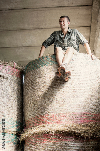 Portrait of young male farmworker on top of haystack in farm barn photo