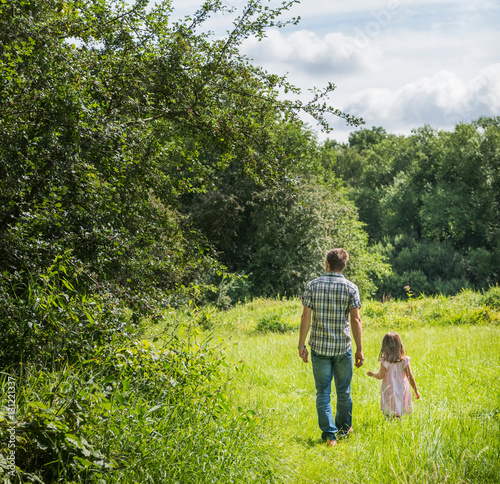 Rear view of father and daughter walking through meadow, Porta Westfalica, North Rhine Westphalia, Germany