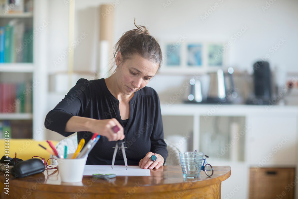 Mature woman sitting at desk, using pair of compasses Mature woman sitting at desk, using pair of compasses