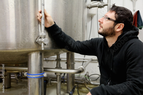 Worker in brewery, checking pressure gauge on brew tank