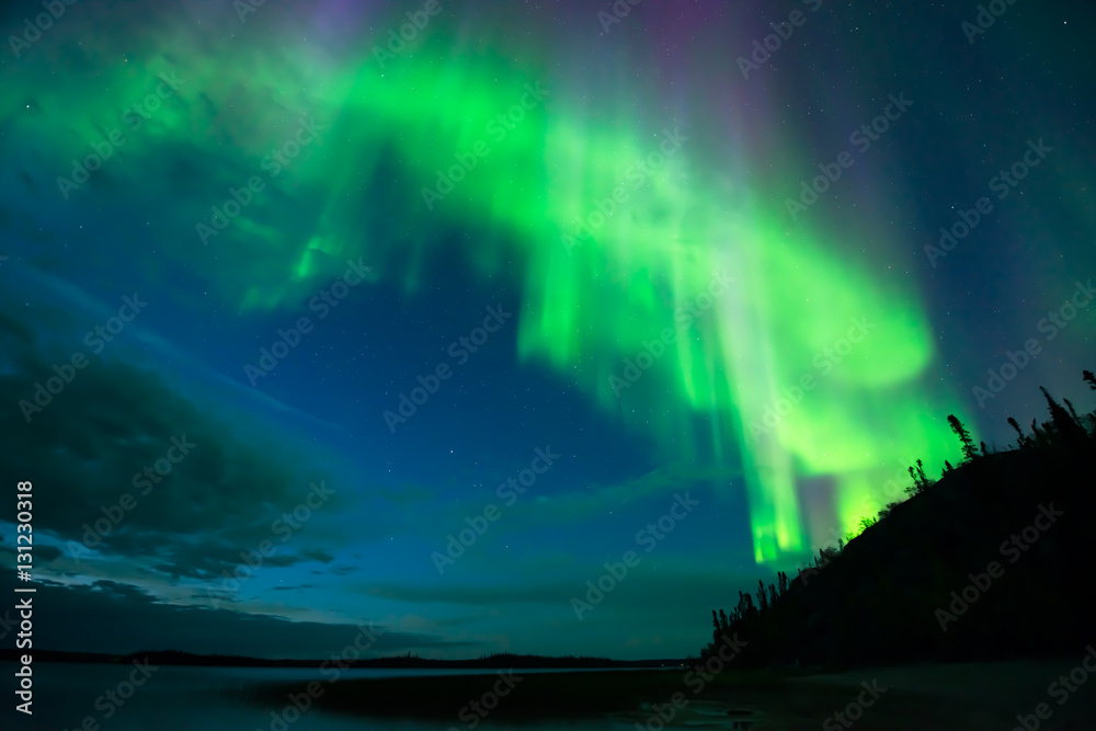 Aurora on Lake - Bright cloud-shape aurora borealis beam down over a lake from the starry night sky.