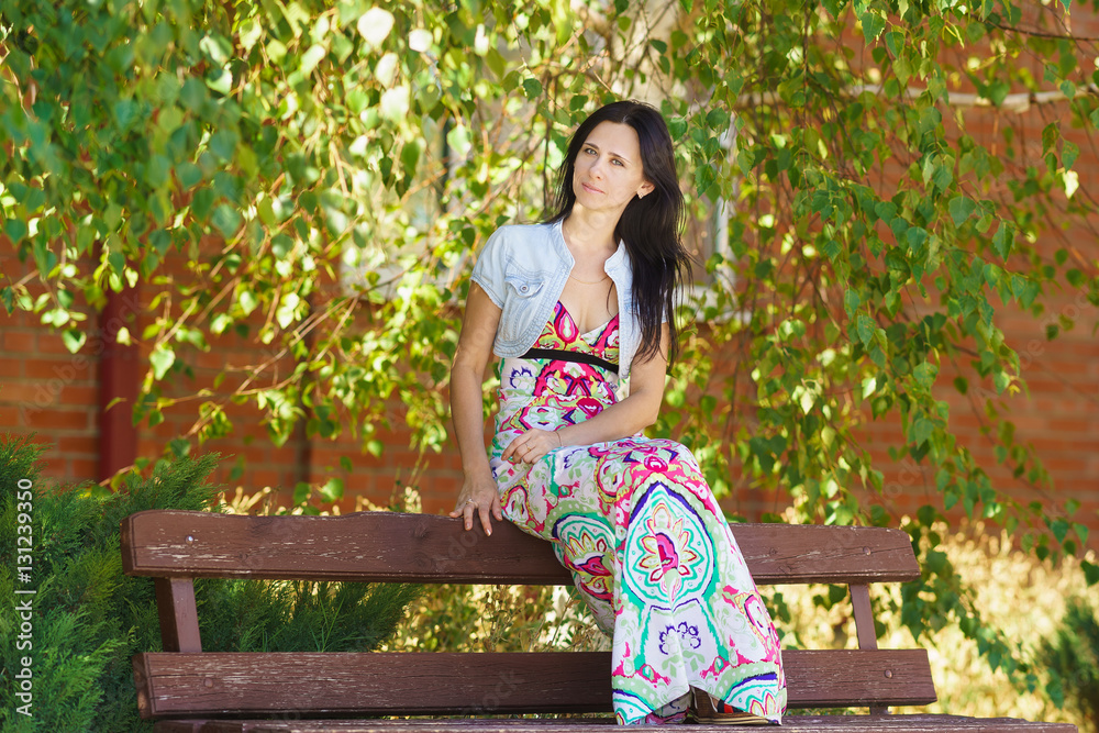 Fototapeta premium Happy beautiful young woman sitting on a bench near the tree